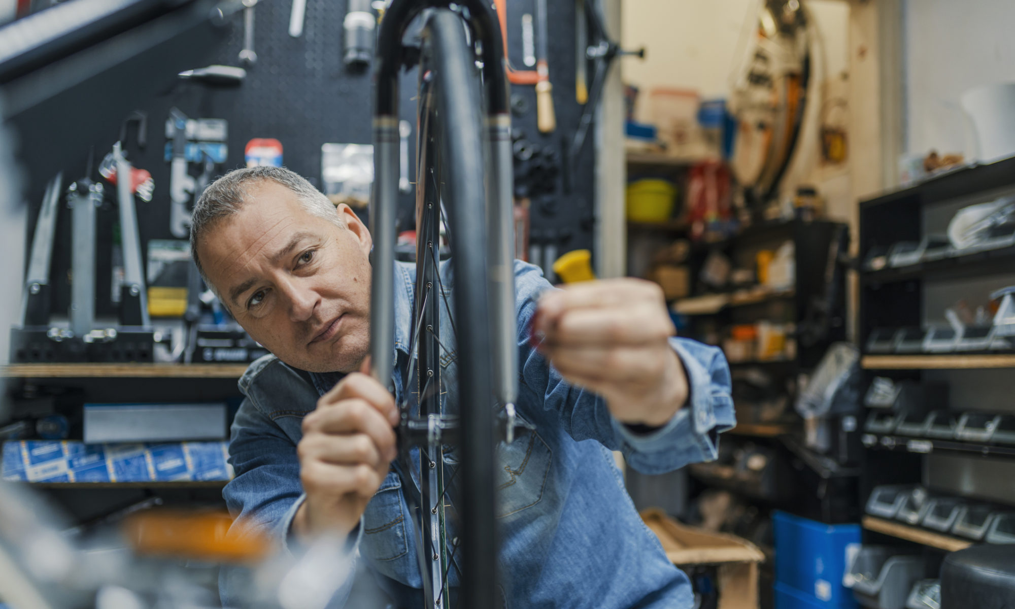 Male dressed in blue fixing a bicycle in a bicycle shop