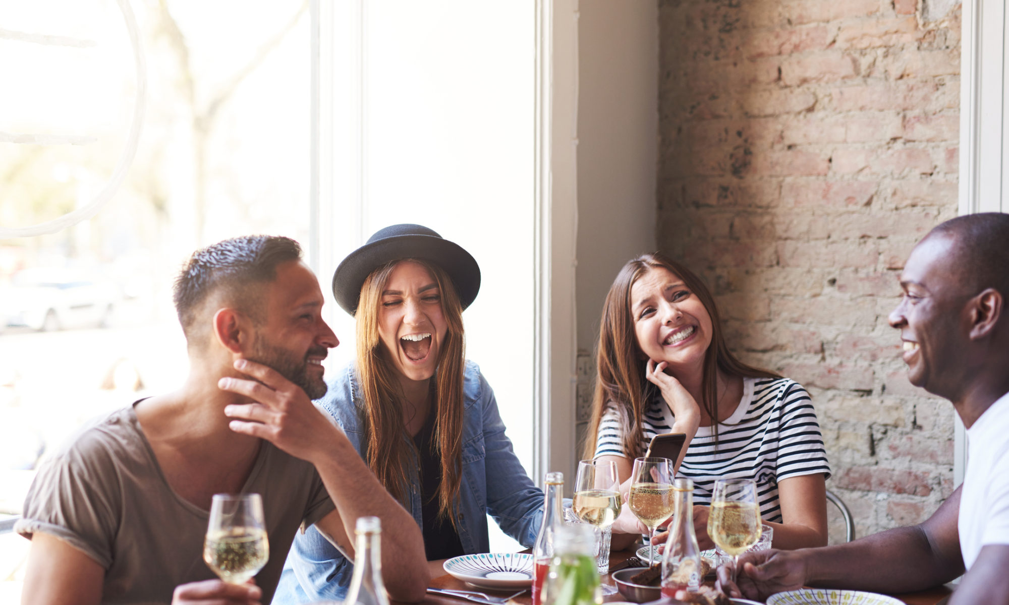 Diverse small group of four attractive laughing friends having wine and a meal together in restaurant talking about how much it cost to make a website for a small restaurant