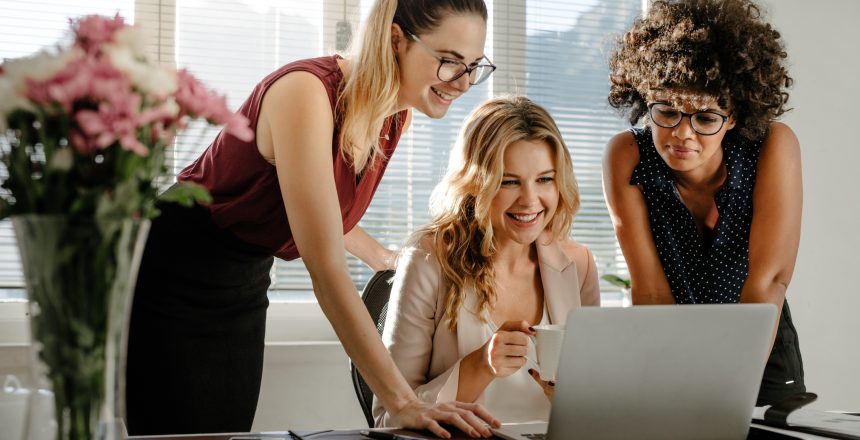 Three businesswomen looking at laptop and smiling as they have confirmed the privacy policy statement on website