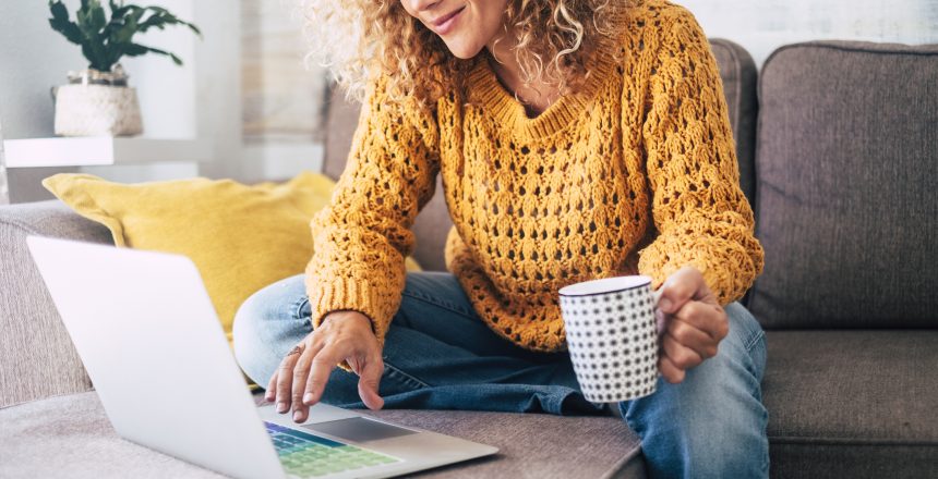 Female small business owner sat on her sofa at home with a hot coffee planning her SEO strategy on her laptop. She is casually dressed and smiling