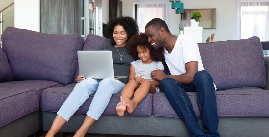 Happy African American family with daughter using laptop at home, shopping online and reading how online shopping websites work
