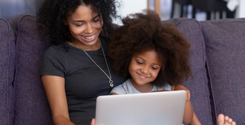 Smiling african american mother and kid daughter having fun with computer looking at her personal website