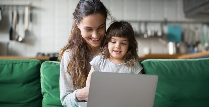 Female sat on a green sofa with a child and a laptop on her lap