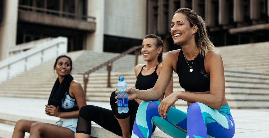 Group of three females sitting on steps outside and relaxing after running in their sports club