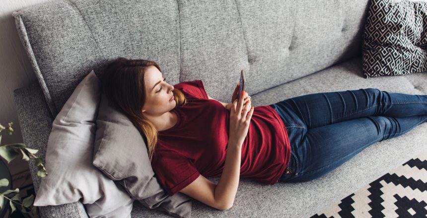 Female relaxing on a grey sofa whilst using her mobile phone to run her business from home