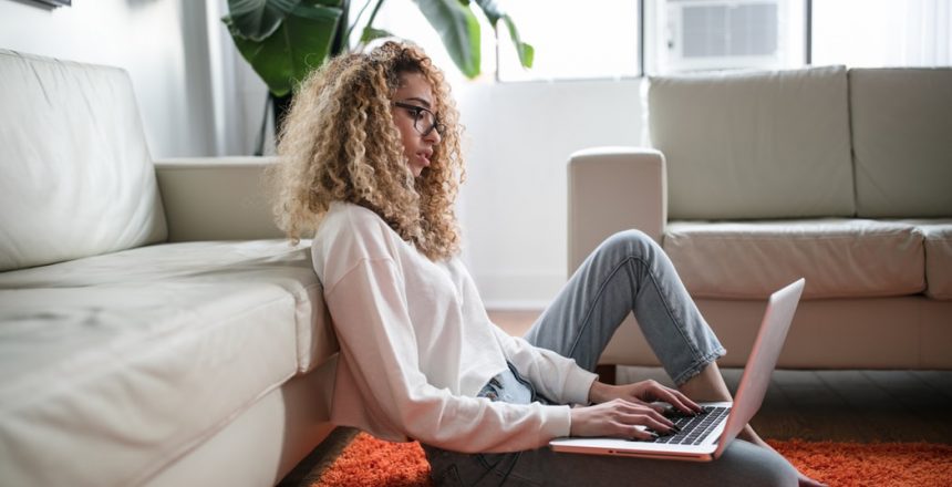 Female sitting on the floor up against her sofa working on her laptop